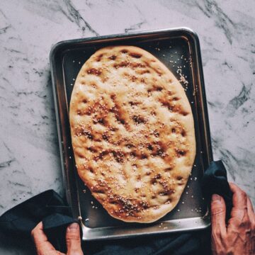 2 hands holding a baking tray with a freshly baked flatbread