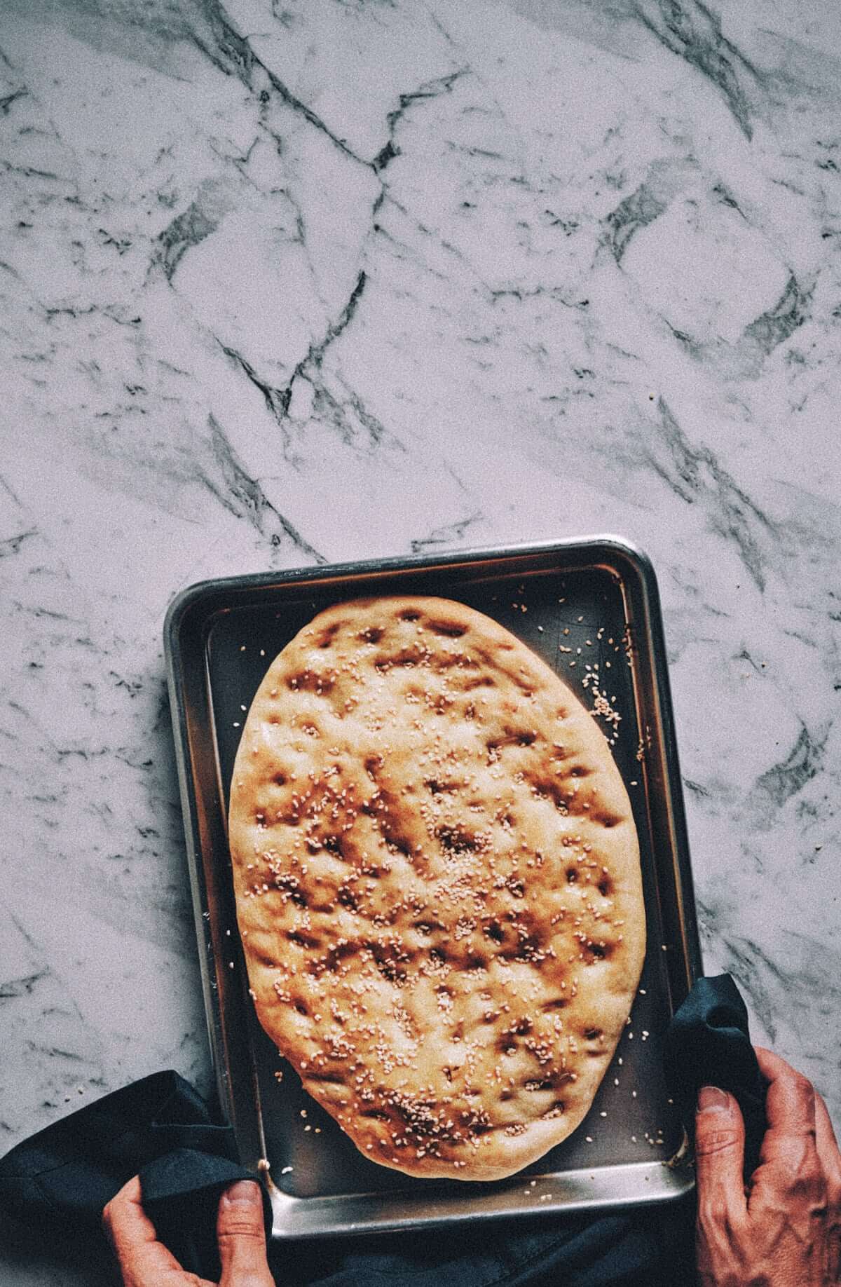 freshly baked bread on a baking tray being handled by two hands with a kitchen towel