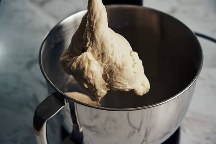 kneaded dough hanging form a dough hook on a stand mixer