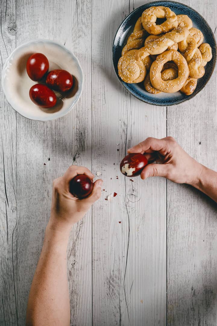 2 hands cracking eggs on a white table with a plate of biscuits on it too