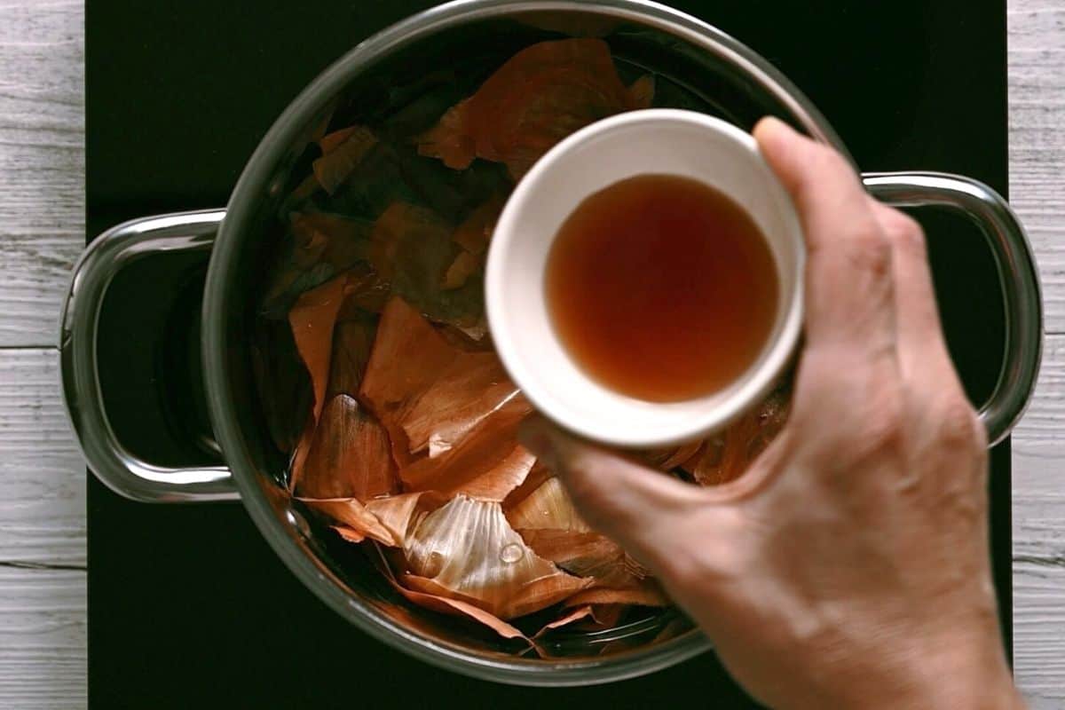 pouring vinegar into a pot filled with onion skins