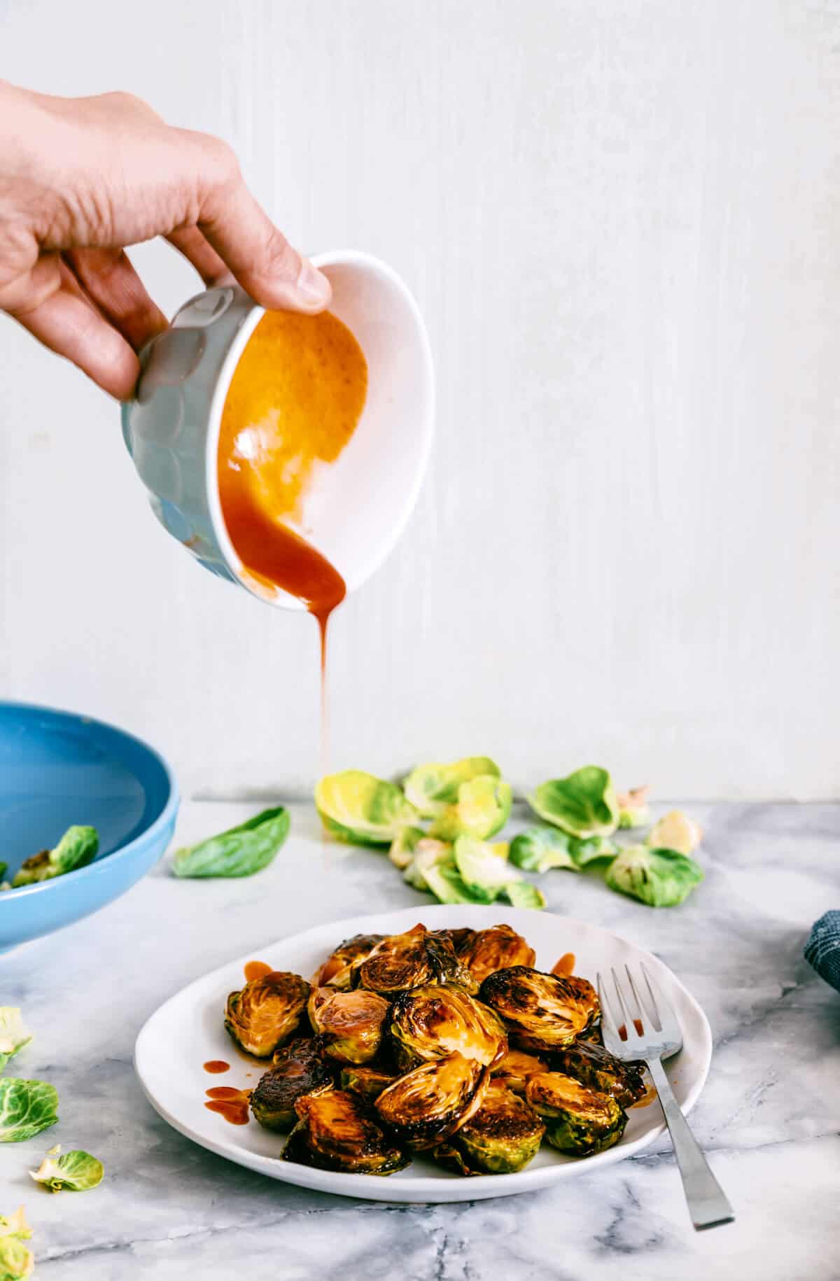 hand pouring honey sriracha sauce over roasted brussel sprouts.