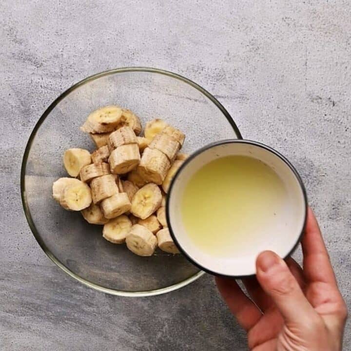 pouring lime juice over chopped bananas in a glass bowl