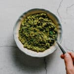 hand holding a spoon in a bowl of parsley walnut pesto.