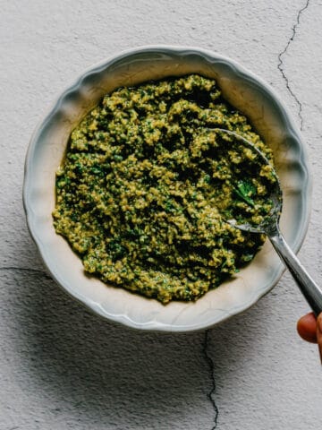 hand holding a spoon in a bowl of parsley walnut pesto.