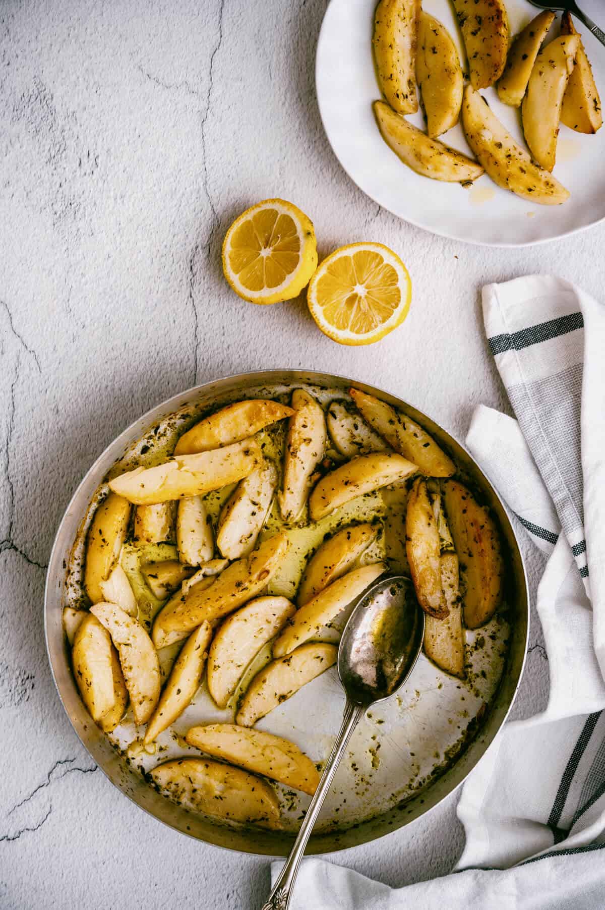 vertical shot of a round silver pan of roasted greek potatoes with lemon and oregano.