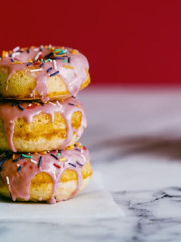 3 strawberry frosted doughnuts stacked on top of each other.