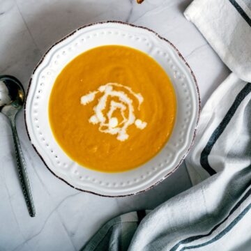 overhead shot of a white scalloped bowl filled with carrot and orange soup drizzled with some heavy cream.
