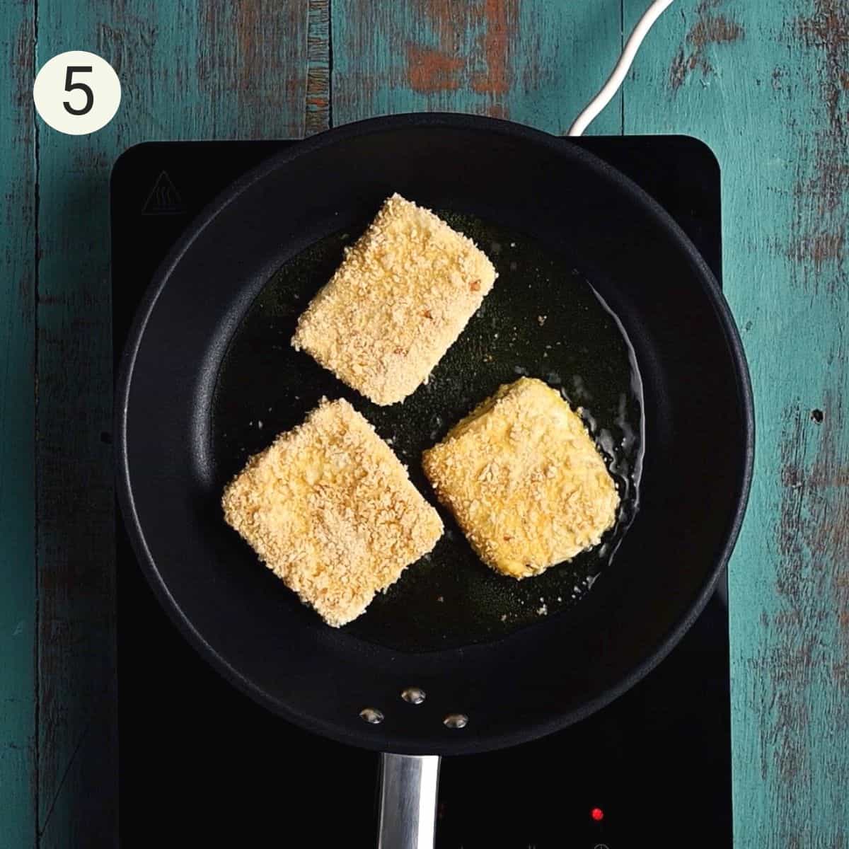 3 pieces of halloumi being fried in a pan with olive oil.