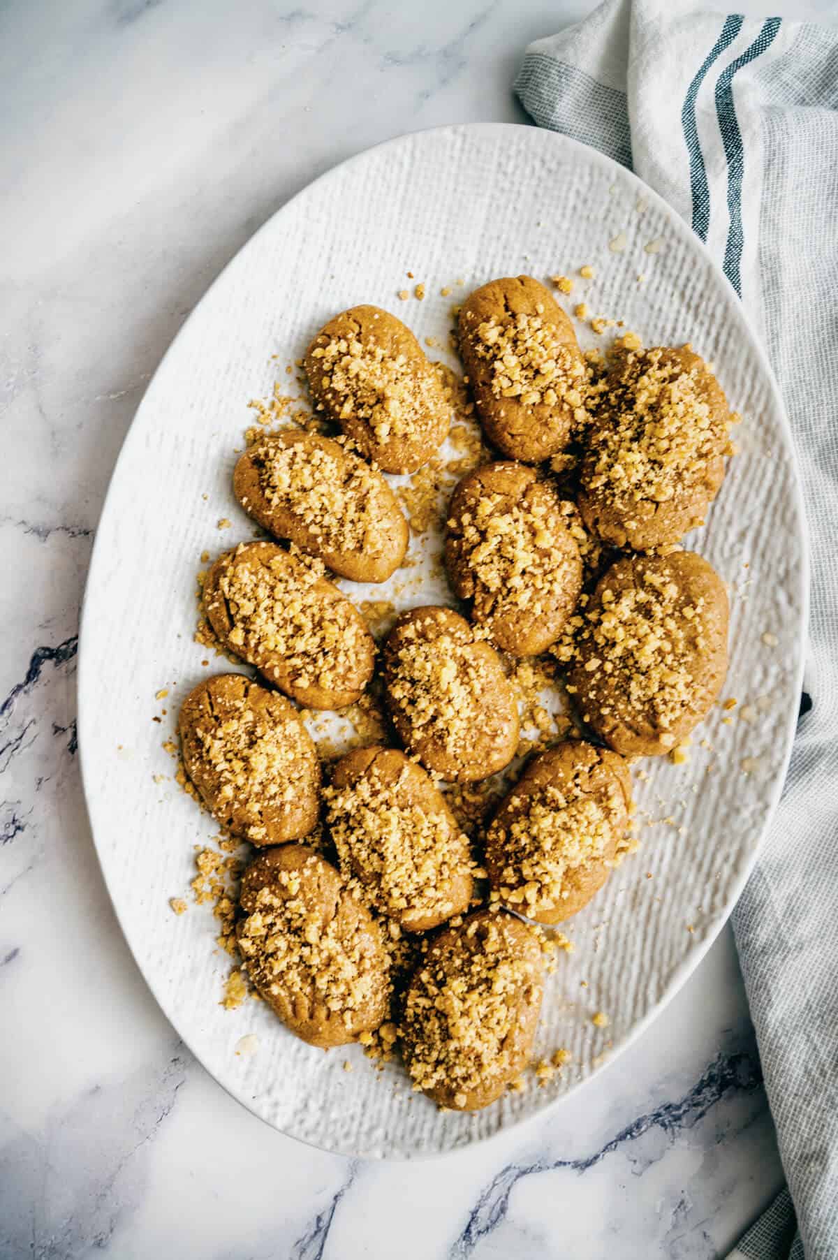 a white plate filled with Greek honey cookies topped with walnuts.
