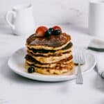 a stack of almond flour pancakes topped with fruit and drizzled with maple syrup.