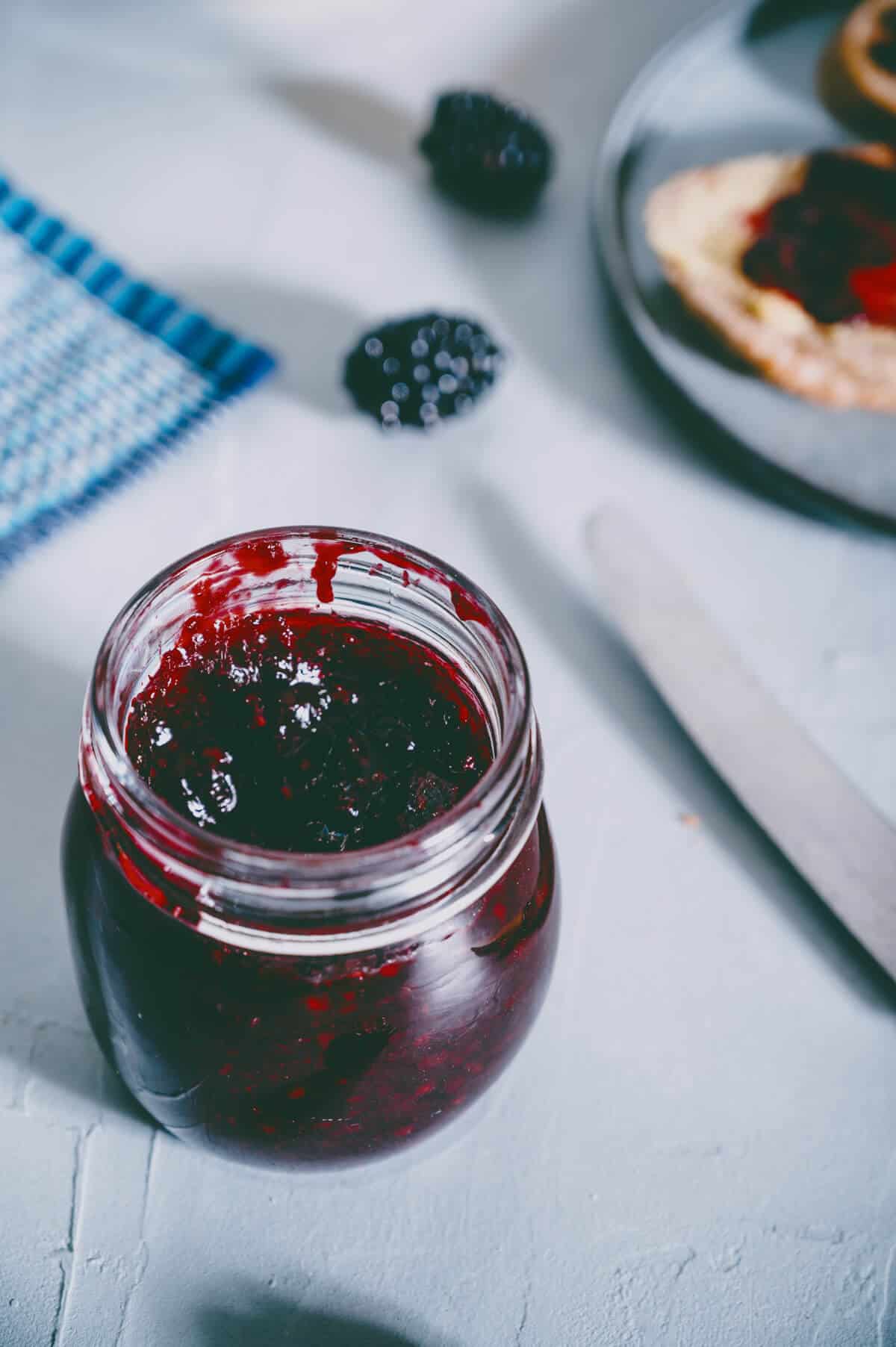 a jar of homemade blackberry jam on a grey table.