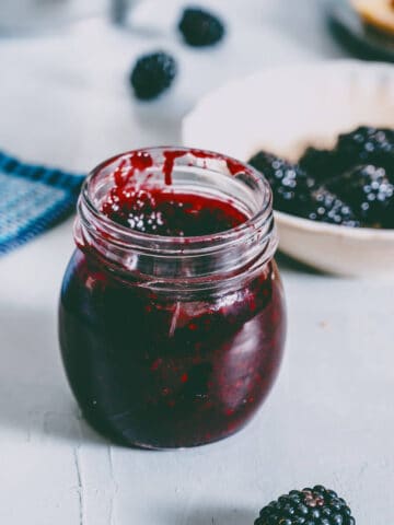 a jar of homemade blackberry jam on a grey table.