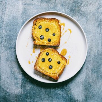 yogurt filled toast topped with blueberries and honey on a white plate.