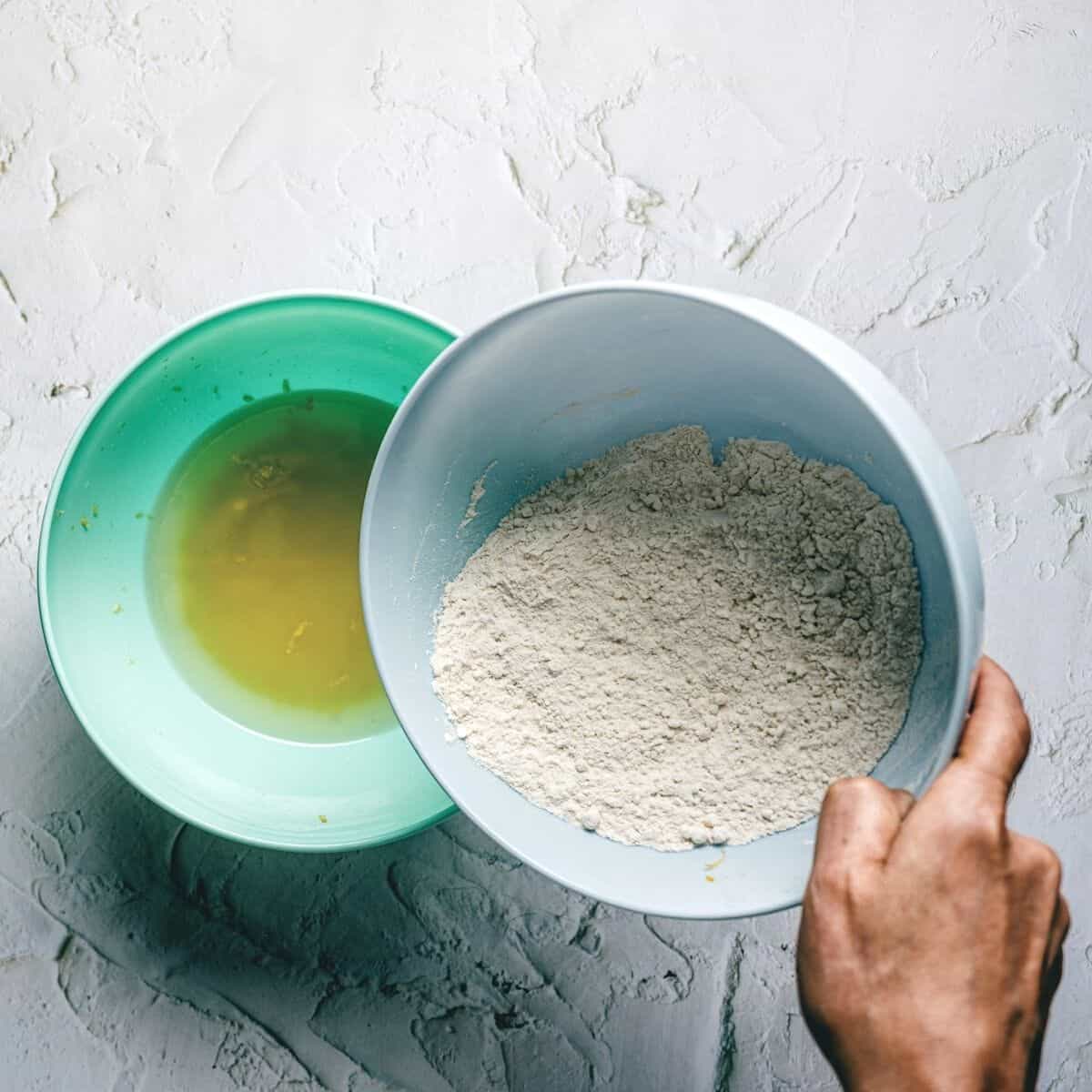 pouring flour to a green bowl filled with olive oil and sugar.