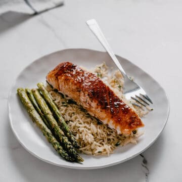 a white plate with rice with cooked salmon and asparagus.