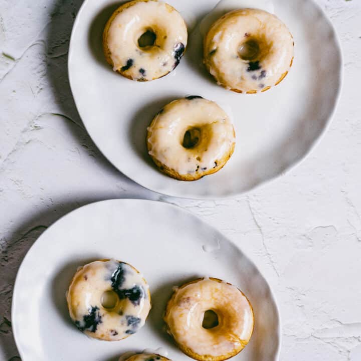 2 white plates with glazed blueberry cake donuts.