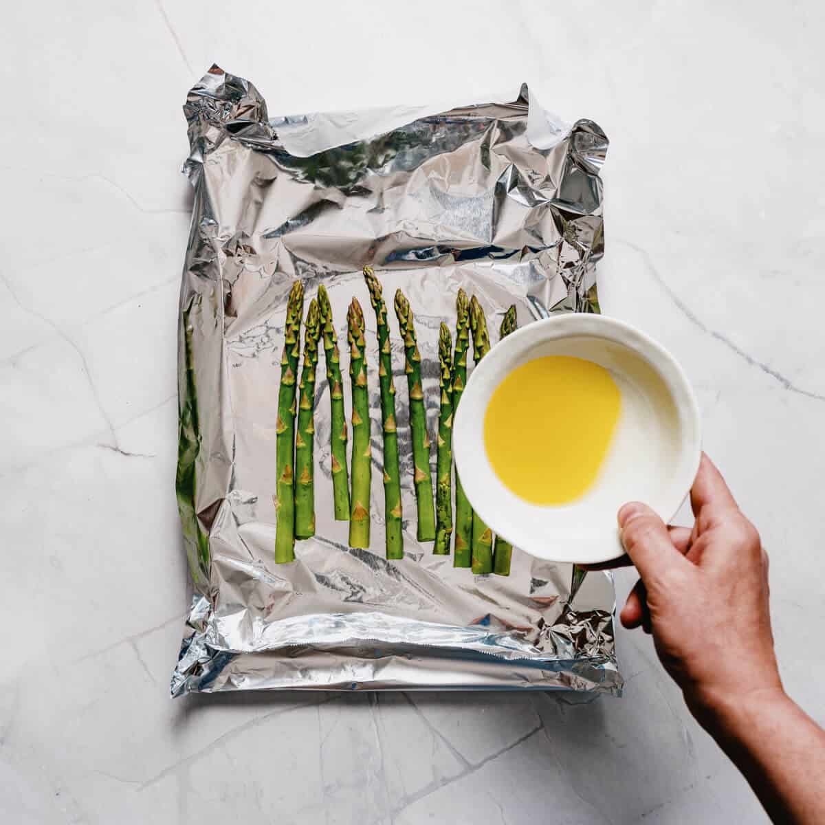 drizzling olive oil over asparagus spears in aluminum foil.