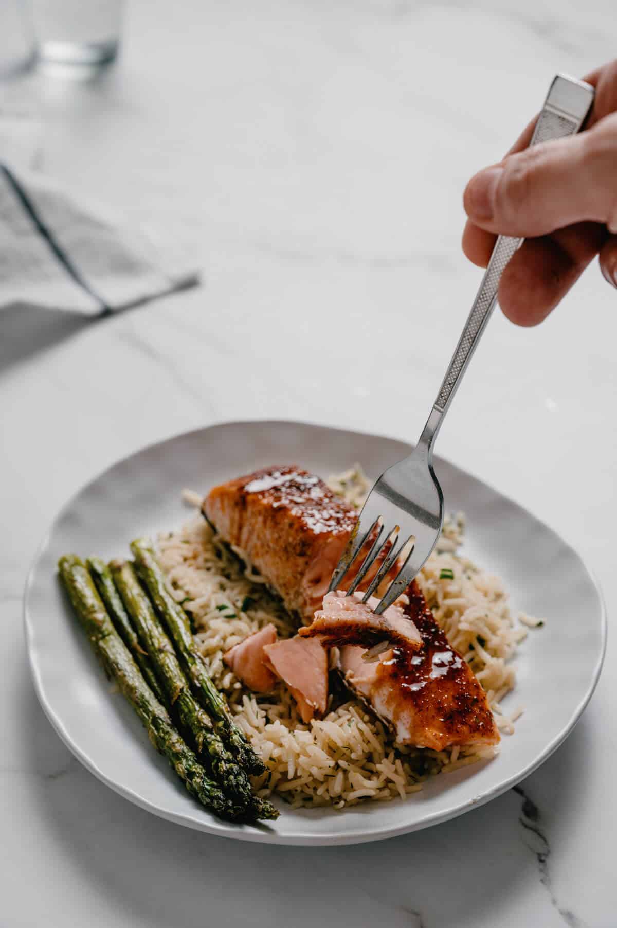 a fork flaking cooked salmon on a plate with rice and asparagus.