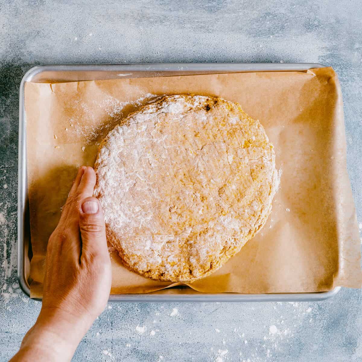 shaping pumpkin scone dough into a disc on a baking sheet.