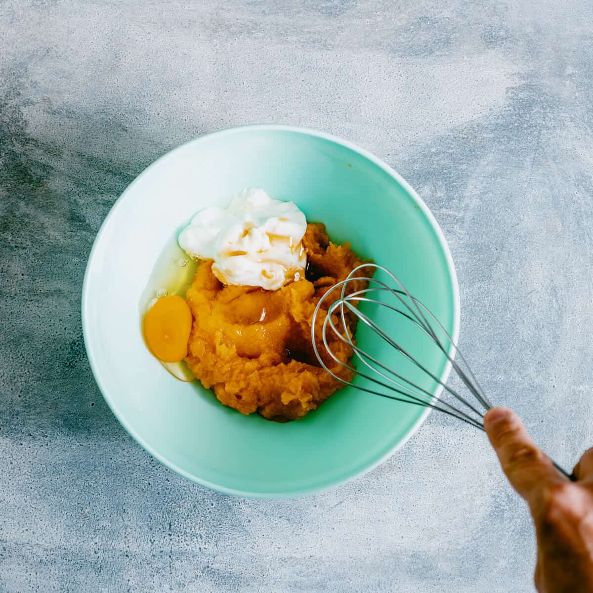 mixing pumpkin, vanilla and eggs in a green bowl with a whisk.