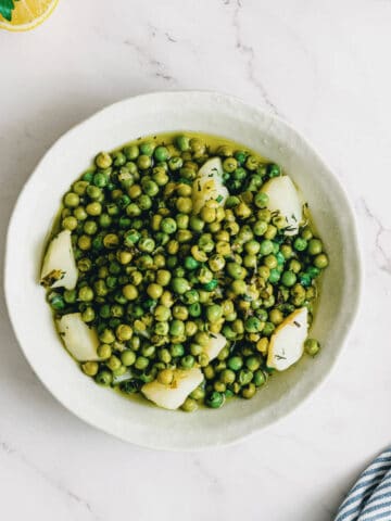 a bowl of green peas with potatoes on a white table.