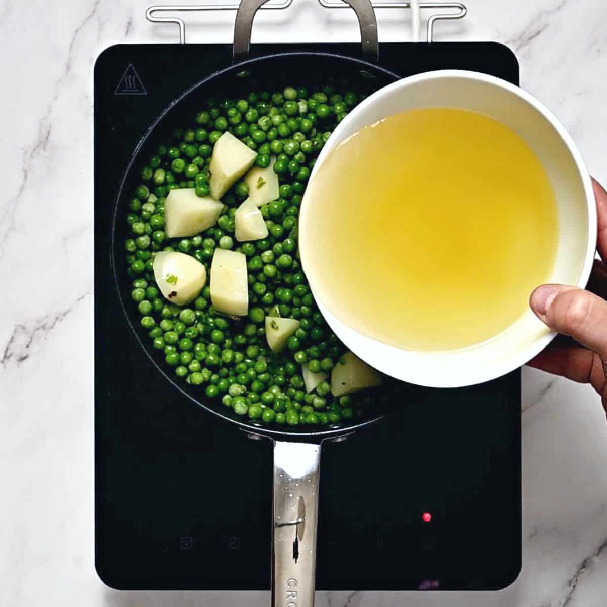pouring stock to green peas in a skillet.