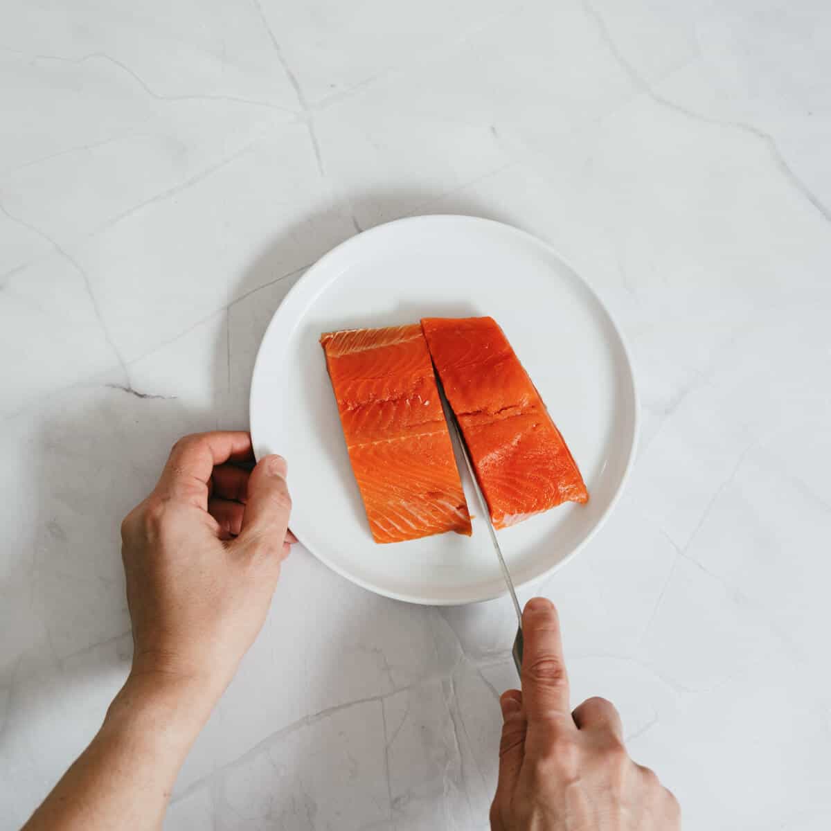 cutting salmon fillets in half on a white plate.