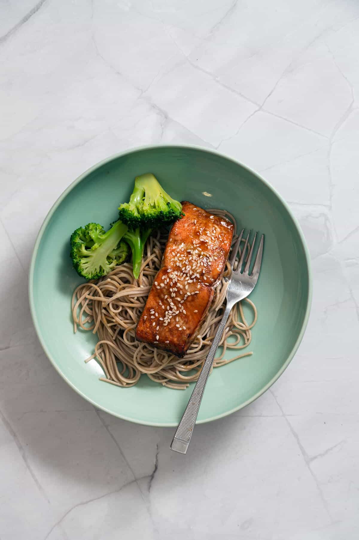 honey garlic salmon cooked in an air fryer in a green bowl with noodles and broccoli.