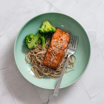 honey garlic salmon cooked in an air fryer in a green bowl with noodles and broccoli.