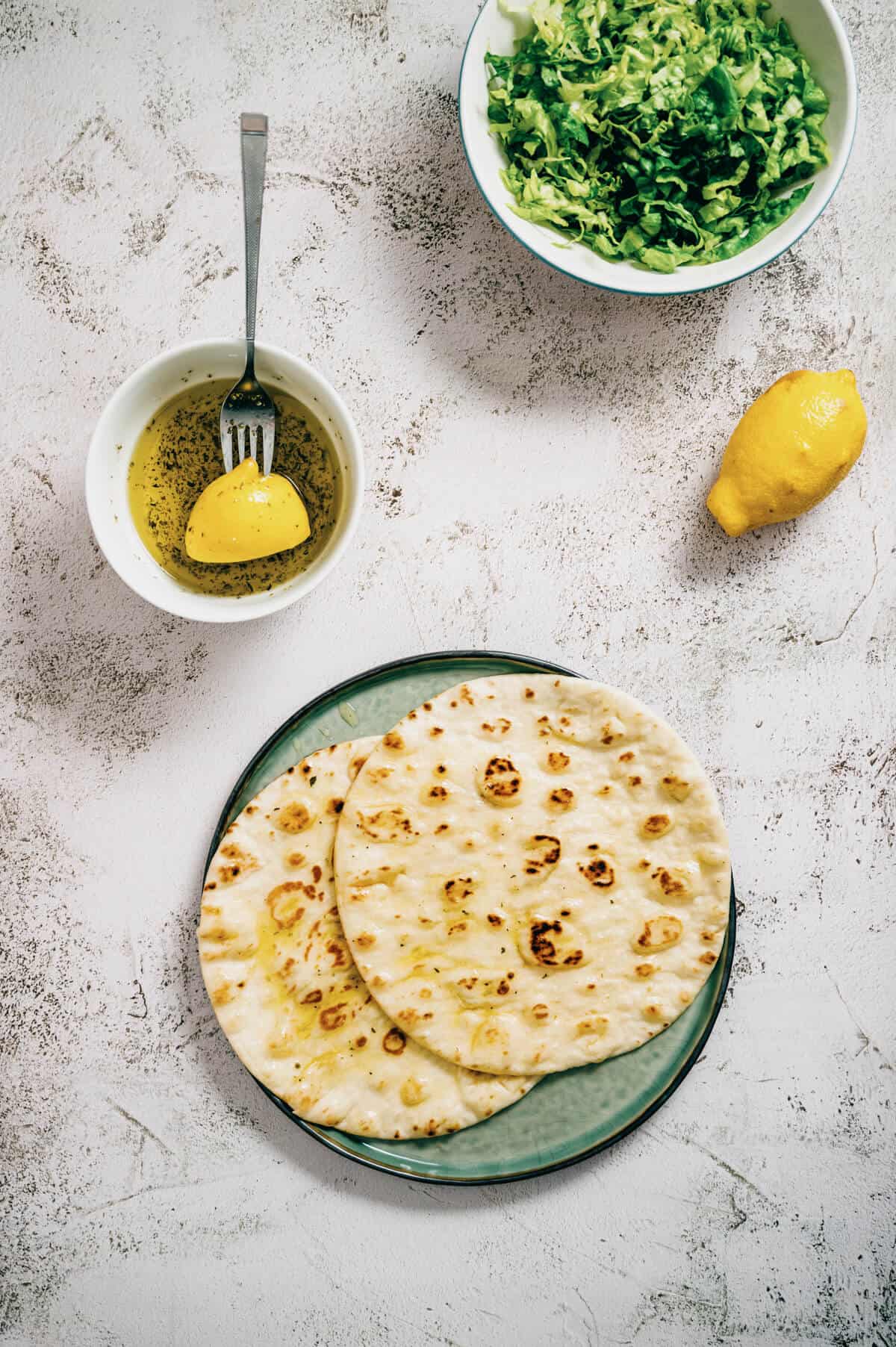 pita breads on a table with olive oil and salad.