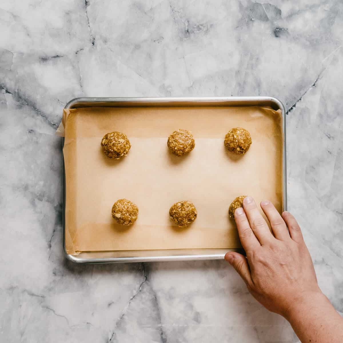 flattening unbaked Anzac biscuits on a baking tray.