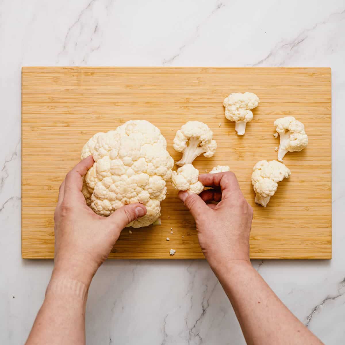 separating cauliflower florets on a wooden chopping board.