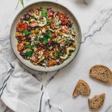 Greek lentil salad in a bowl with bread on a marble table.