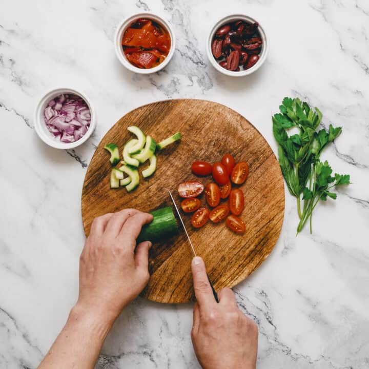 chopping ingredients on a round cutting board to make Greek lentil salad.