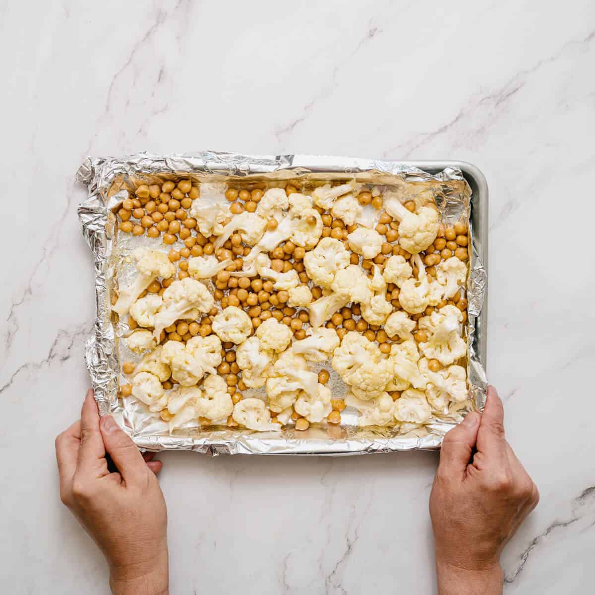 cauliflower florets and chickpeas on a lined baking tray.