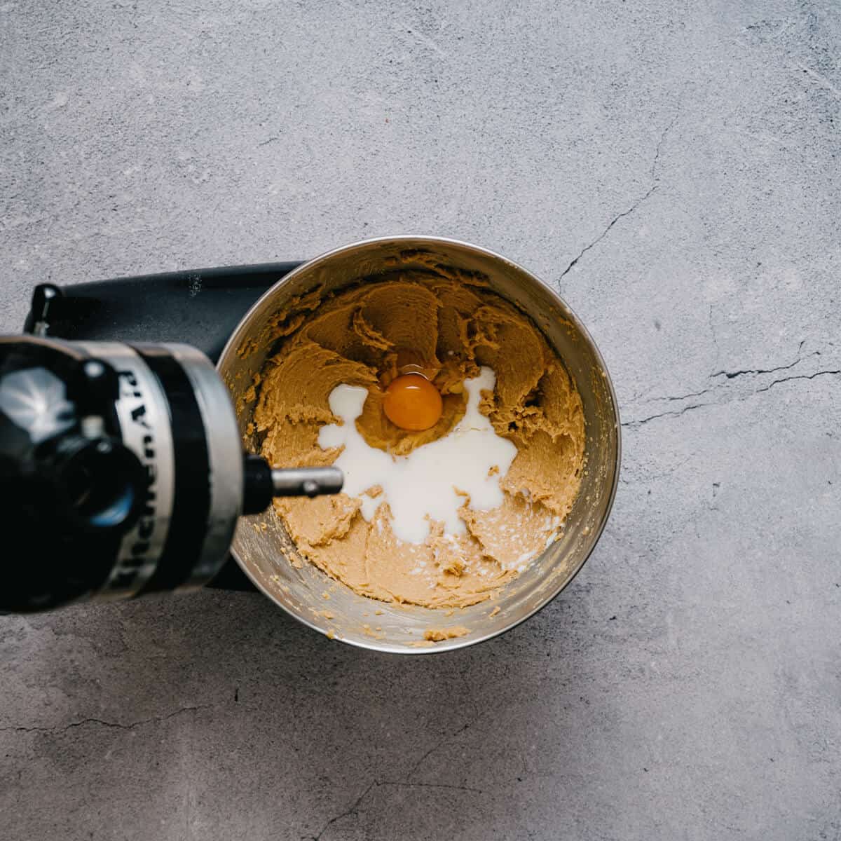 adding an egg and milk to creamed butter in a bowl of a stand mixer.