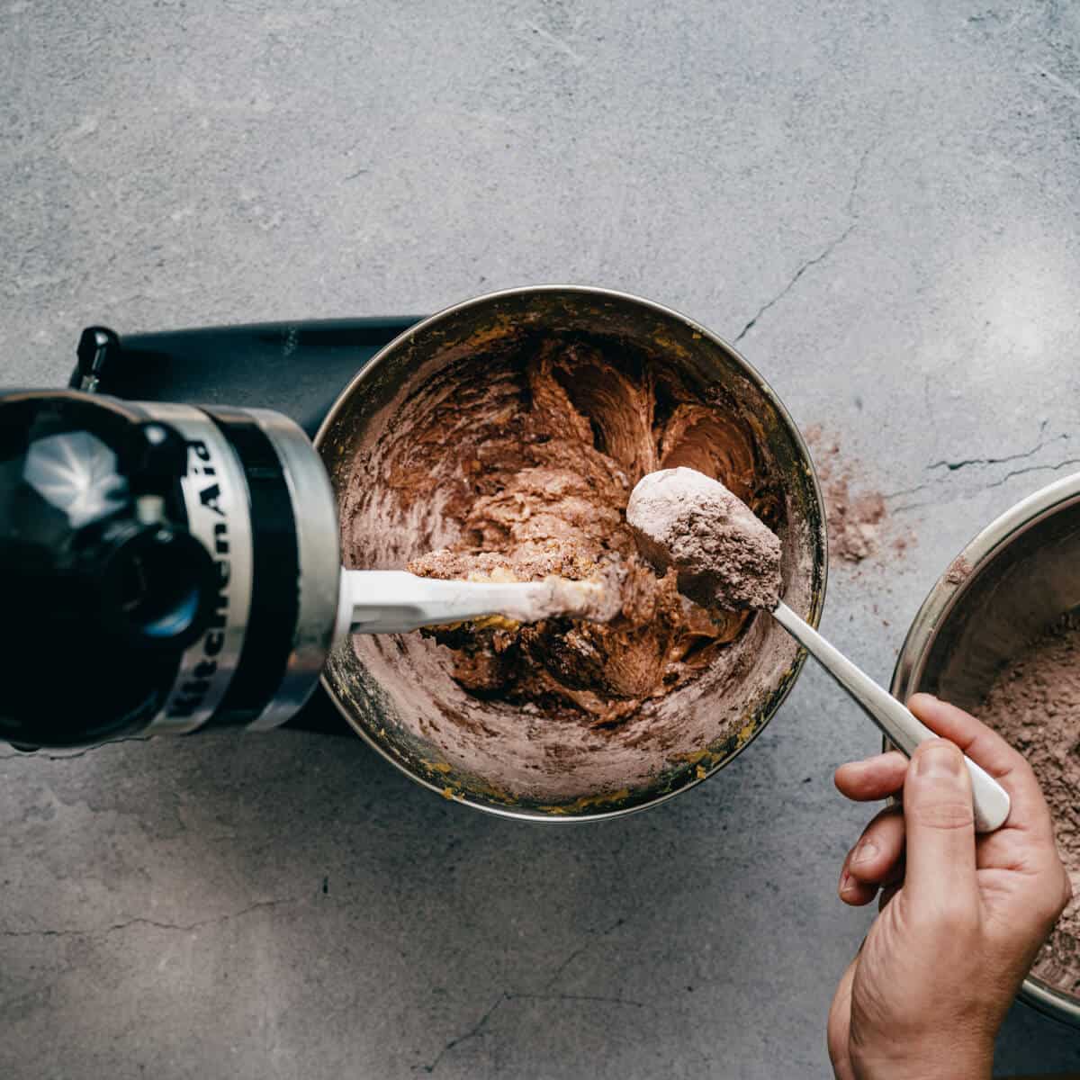 adding flour and cocoa powder to cookie dough in a bowl.
