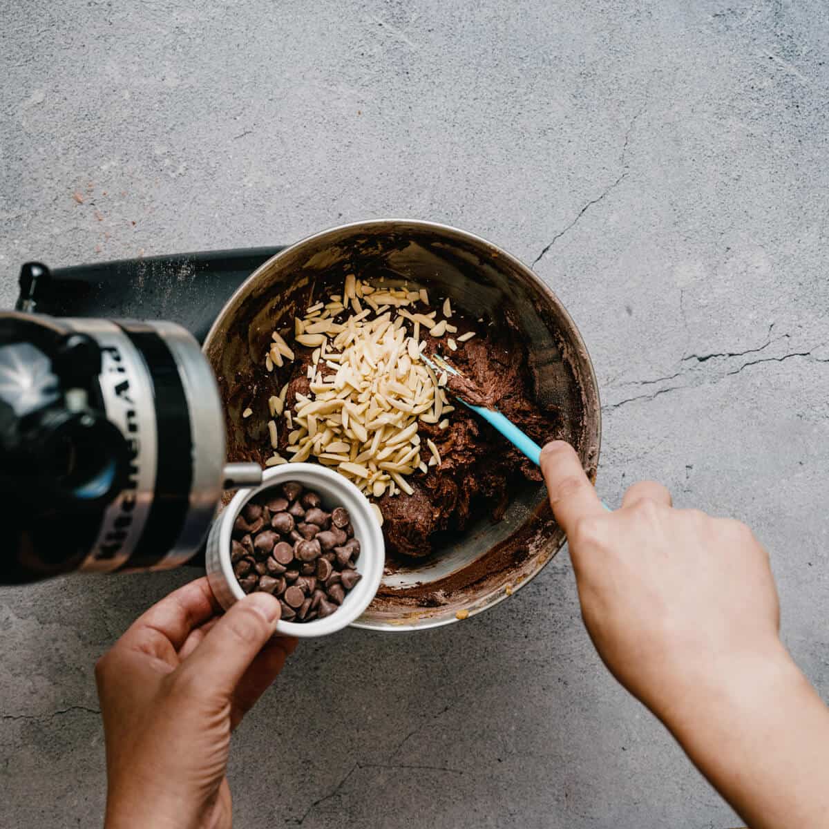 adding almonds and chocolate chips to cookie dough with a spatula.