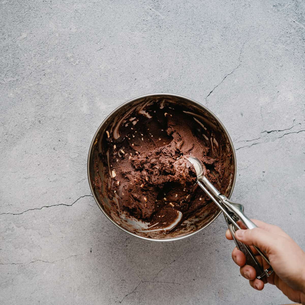 a cookie scoop scooping out chocolate cooking dough from a bowl.