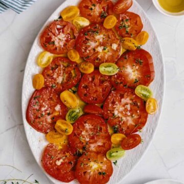 a large white platter on a marble table filled with sliced heirloom tomatoes.