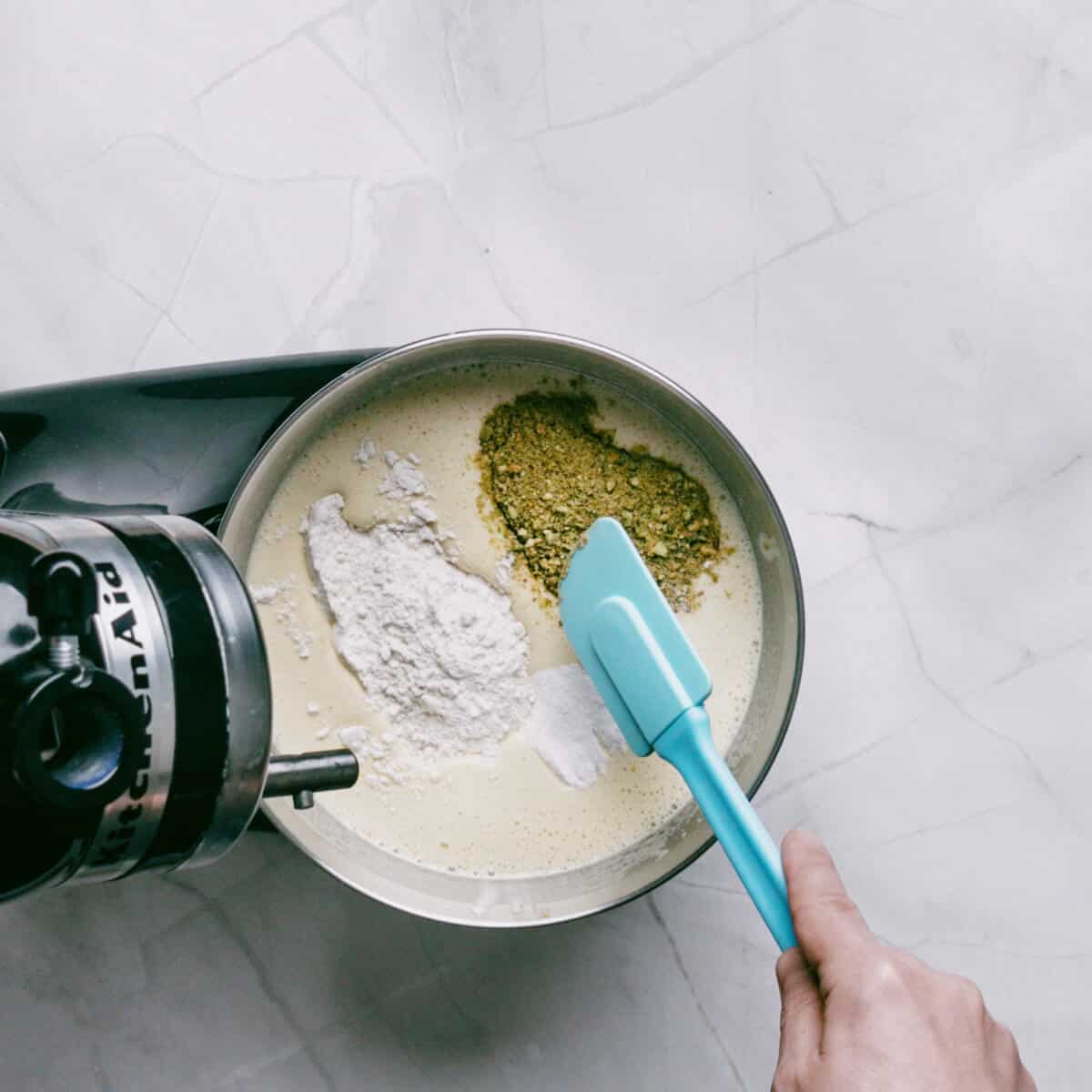 stirring flour and ground pistachios in a bowl of a stand mixer.