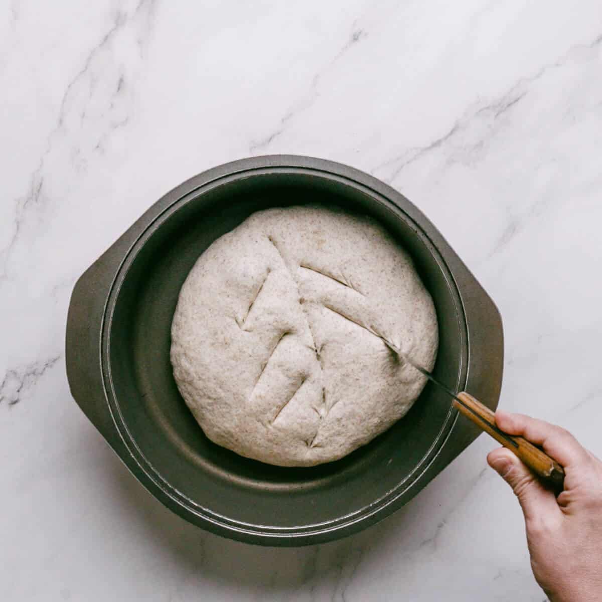 dough being scored in a pre-heated Dutch oven before being baked.