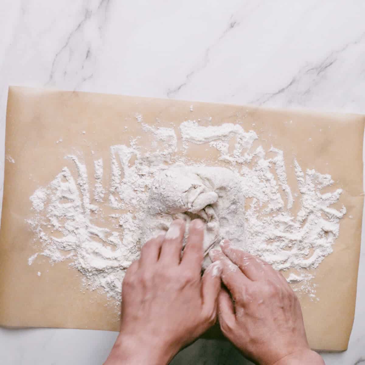 dough being kneaded on a floured surface with parchment paper.