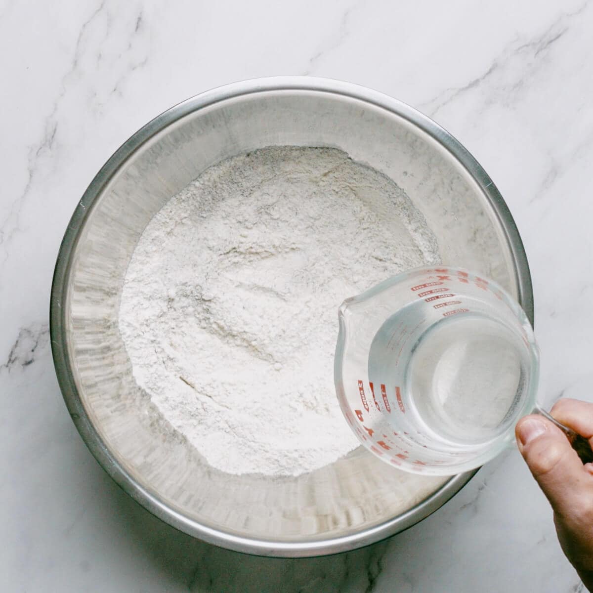 water being poured into a bowl filled with flour.