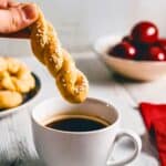 a greek cookie covered in sesame seeds being dunked into coffee.