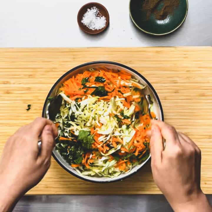 a Greek cabbage salad being tossed in a bowl.