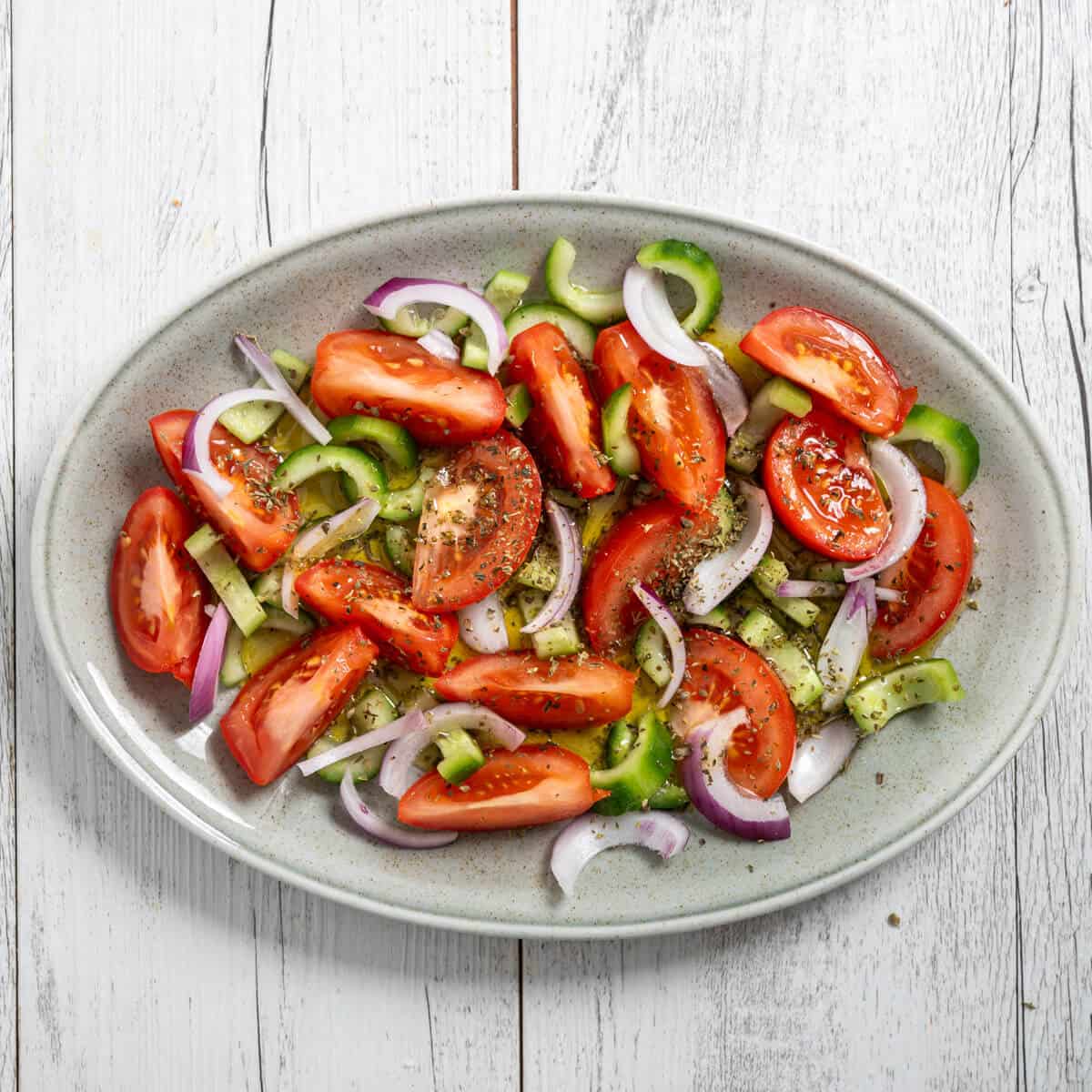 a greek cucumber tomato salad on an oval platter on a white table.