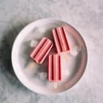 3 strawberry popsicles on a white plate.
