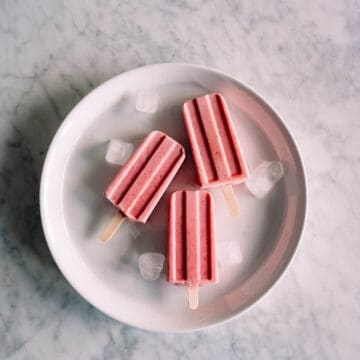 3 strawberry popsicles on a white plate.